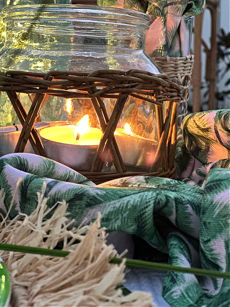 Close up photo of a jar with wicker around it with candles burning inside of it.