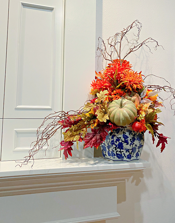 A blue and white porcelain container filled with fall silk flowers and a pumpkin.