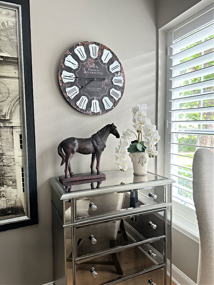 A neutral bedroom with a mirrored chest of drawers a French clock and a horse sculpture.