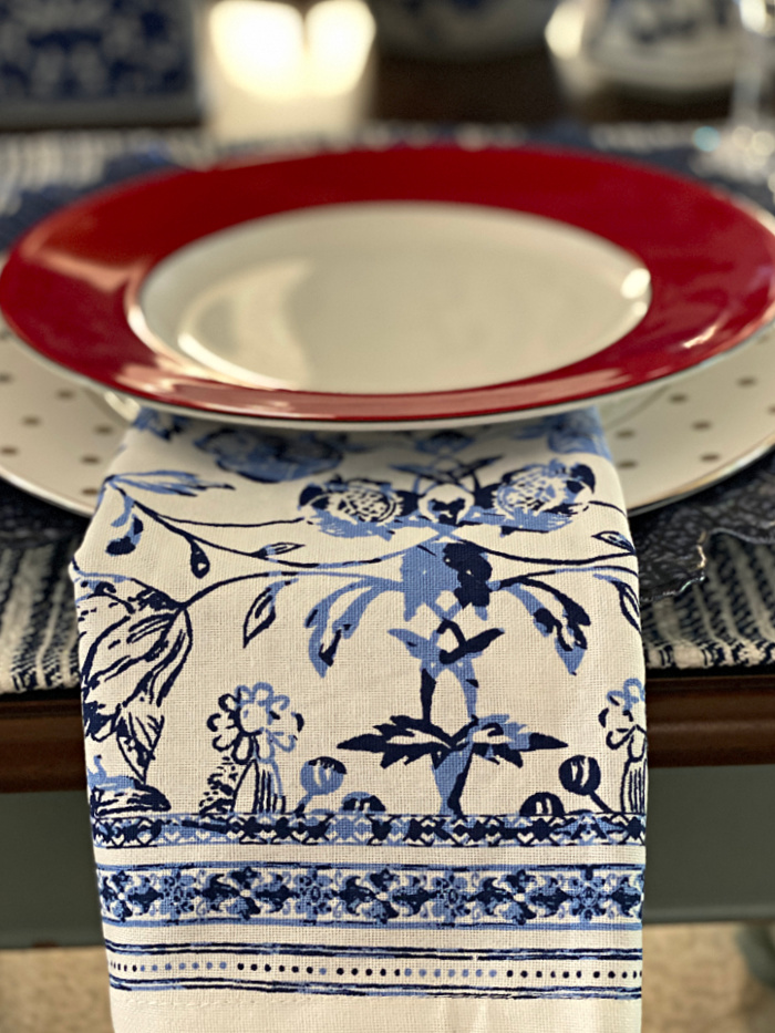 A china plate with silver polka dots and a white plate with a red rim and a blue and white cloth napkin.