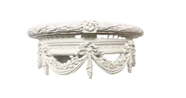 An ornate white carved bed crown with swags on it.