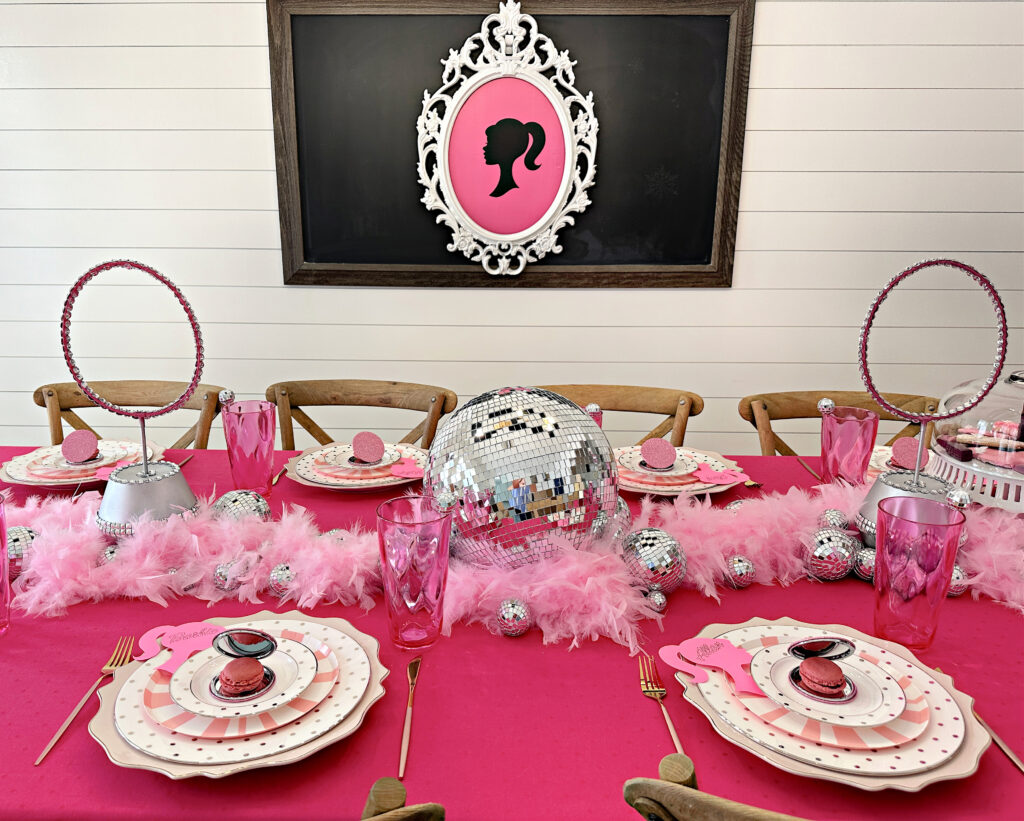 A Barbie themed tablescape in shades of pink and white with mirrored disco balls and pink feather boas for a centerpiece. 