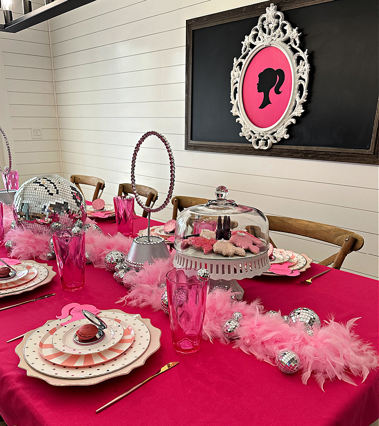 A Barbie themed tablescape in shades of pink and a white frame with a Barbie silhouette on pink.  