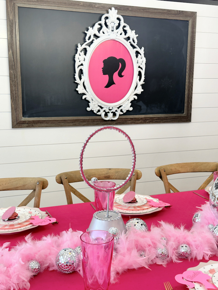 White picture frame with pink background and a black Barbie silhouette  hanging on a chalkboard.  