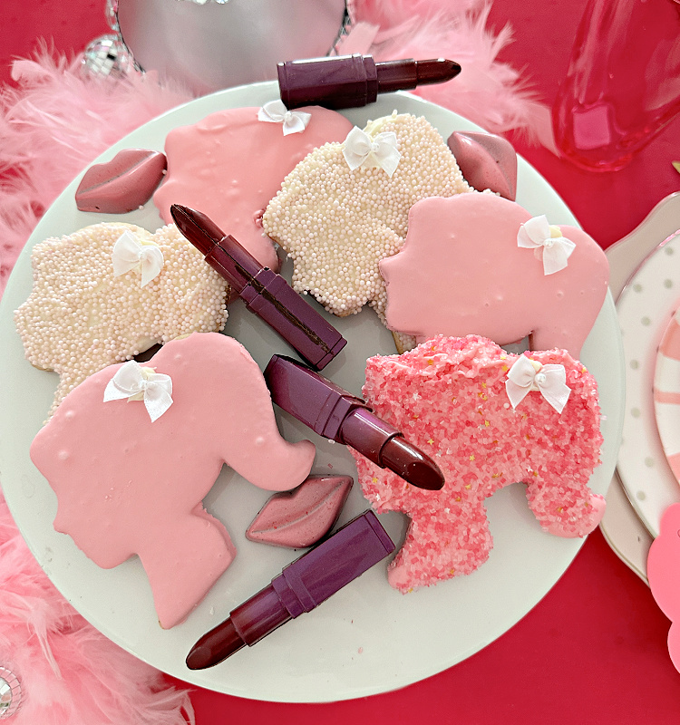 A close up of a plate of Barbie cookies and chocolate lipsticks and pink lips. 