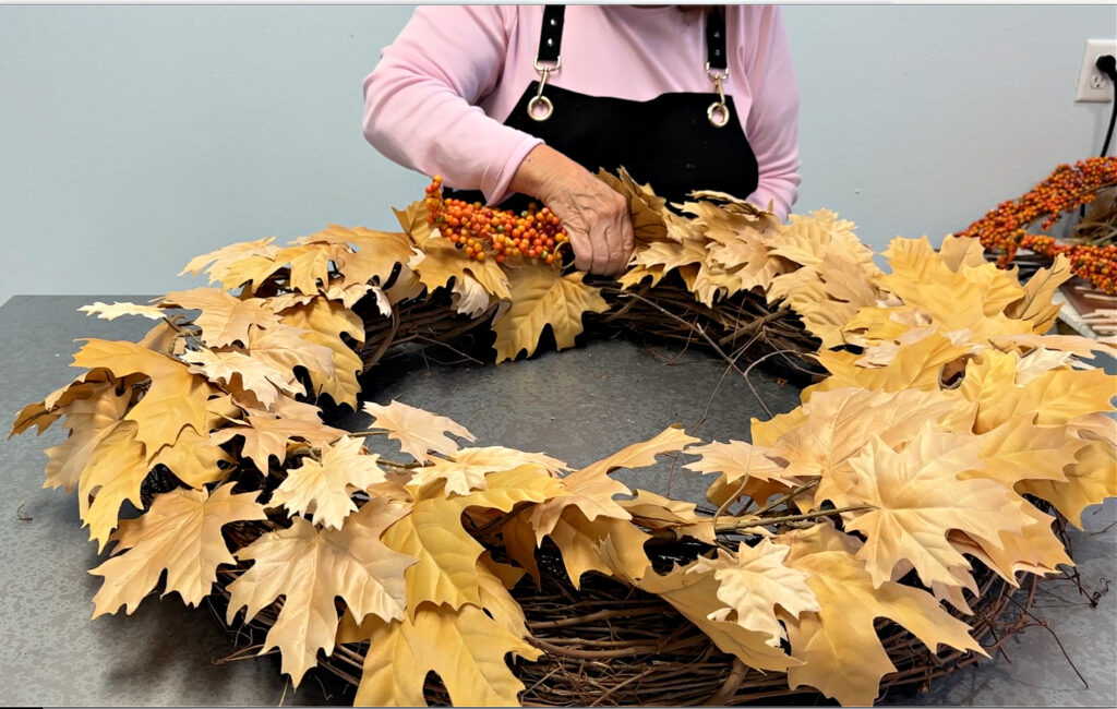 Golden maple leaf wreath with bittersweet clusters being added to the wreath.