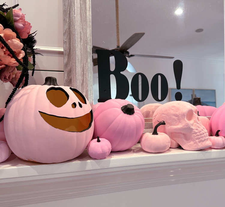A white mantel decorated with pink pumpkins and pink paper bats with two mirrors with the word BOO on each of them.  