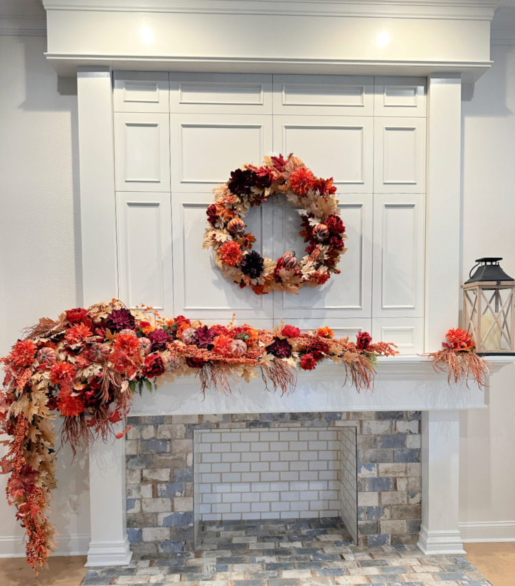 Fall wreath hanging above a mantel with fall faux florals on the mantel and a lantern on the mantel