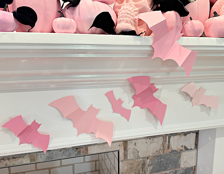 PInk pumpkins on a white mantel and pink paper bats attached to the mantel.