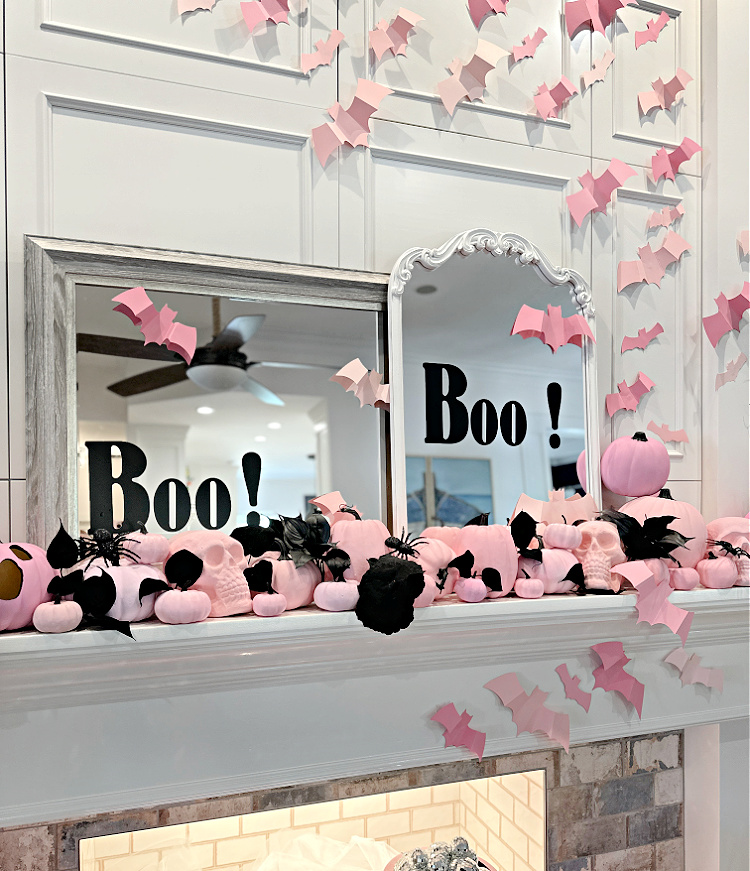 A white mantel decorated with pink pumpkins and pink paper bats with two mirrors with the word BOO on each of them.  