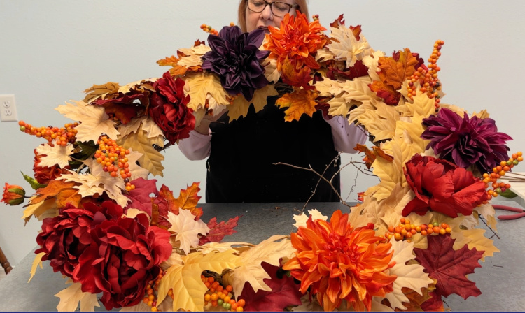 Golden maple leaf wreath with bittersweet berry clusters and fall colored flowers. being help up by a woman