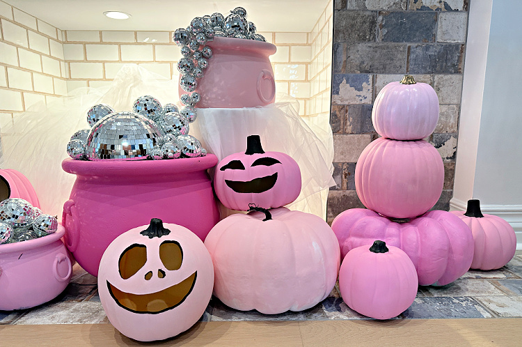 Stack of pink pumpkins and pink jack o lanterns and pink cauldrons with disco balls in the cauldrons.