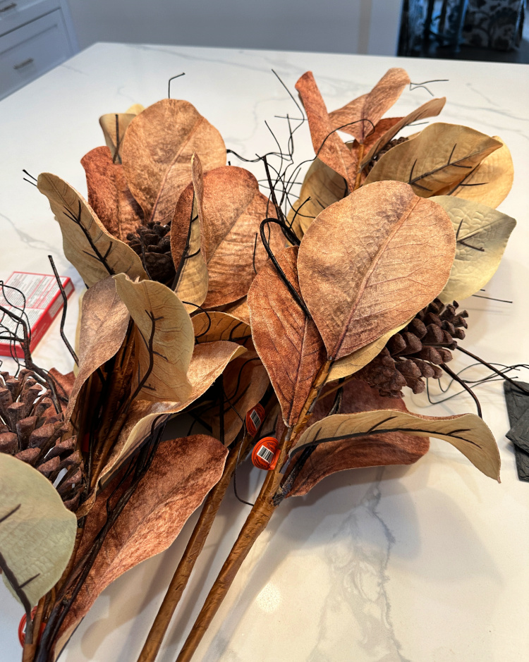Brown and tan faux magnolia leaf branches with pine cones on a kitchen counter.