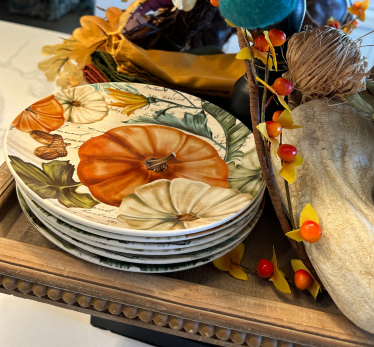 A tiered tray decorated for fall with pumpkin plates, a little plaid stuffed fox, bittersweet garland and seasonal fruits. 