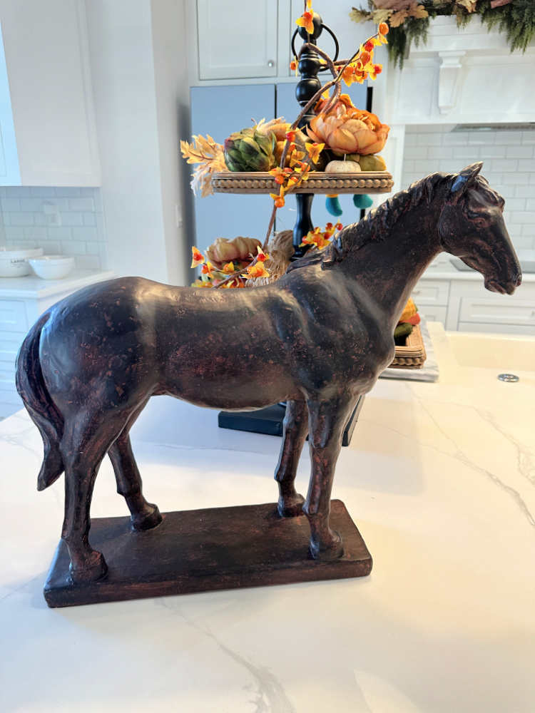 A dark horse statue on a kitchen counter with a fall decorated tiered tray behind it.