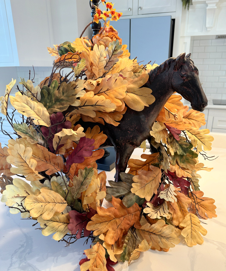 A brown horse state with a fall oak leaf wreath around it. 