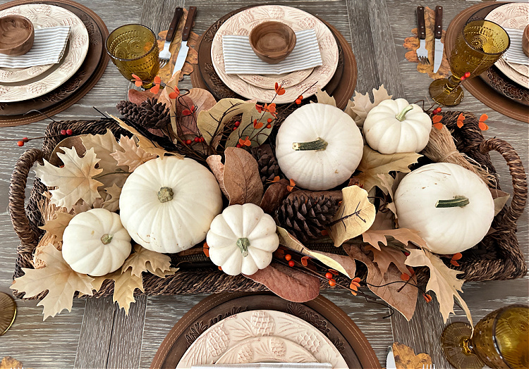 An overhead view of a rectangular basket with white pumpkins, pine cones and golden fall leaves.