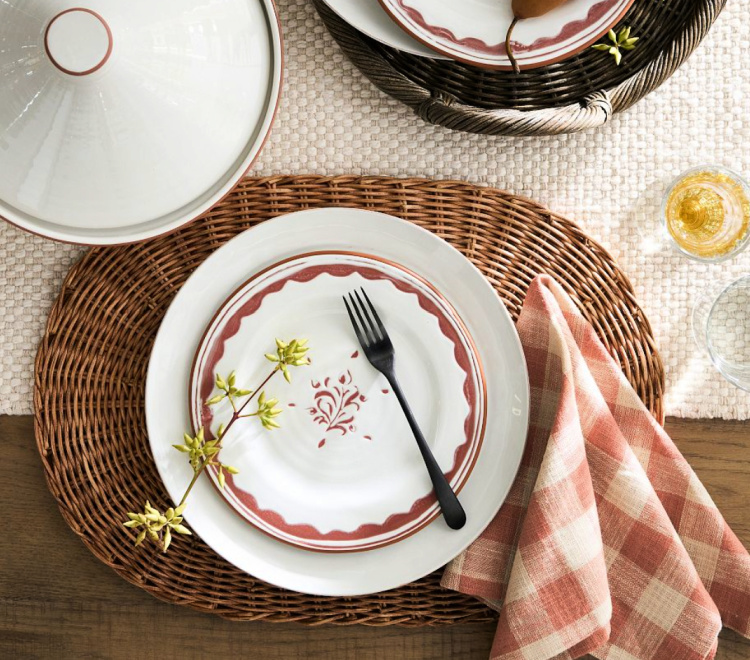 oval wicker placemat with a white plate and orange and white plate on top of that with an orange and white cloth napkin on it.
