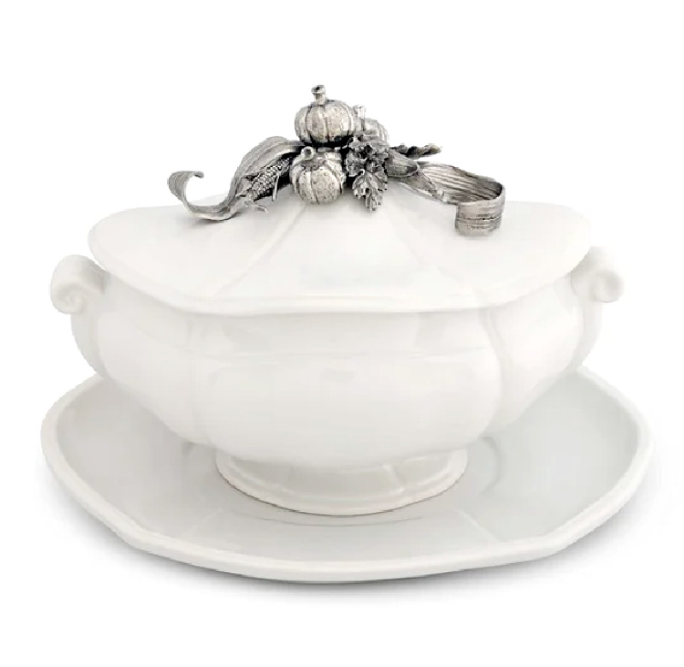 White soup tureen on a white tray with silver embossed pumpkins and fall leaves on the top.