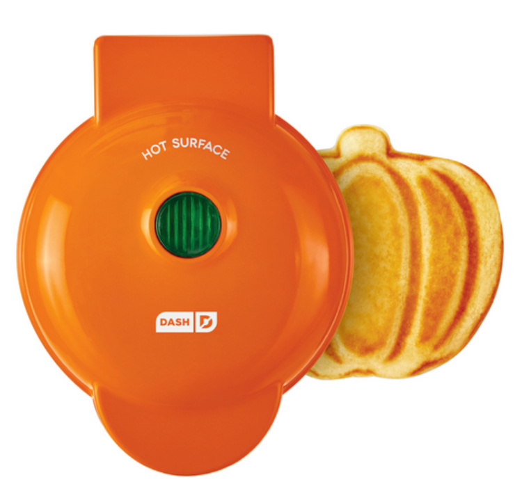 A small orange waffle iron with a small pumpkin shaped waffle next to it.