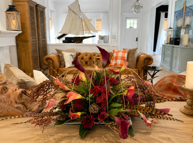 DIY fall pumpkin floral centerpiece created with Dollar Tree wire pumpkin wreath frames, featuring burgundy chrysanthemums, calla lilies, pheasant feathers, and dried botanicals on a rustic farmhouse table.