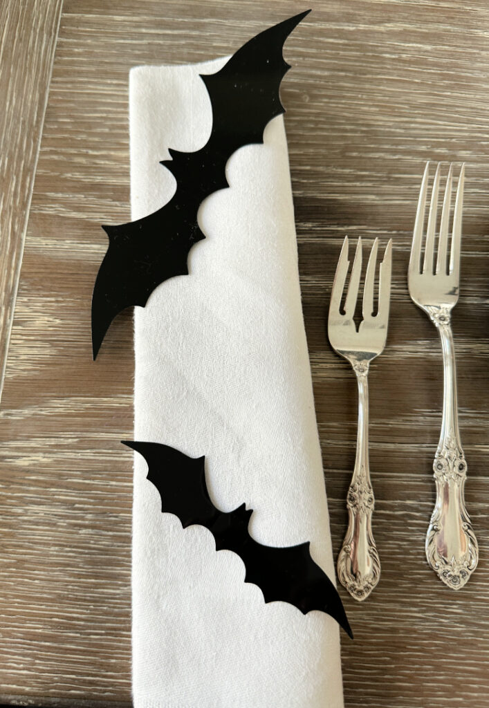 White napkin folded with black bat on it and two silver forks.