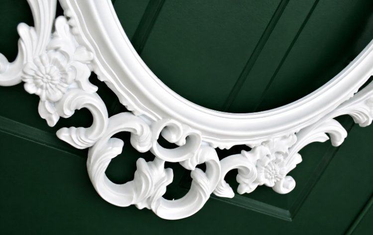 Close up of Ornate white picture frame mounted on a dark green front door, creating the base for a DIY picture frame wreath.