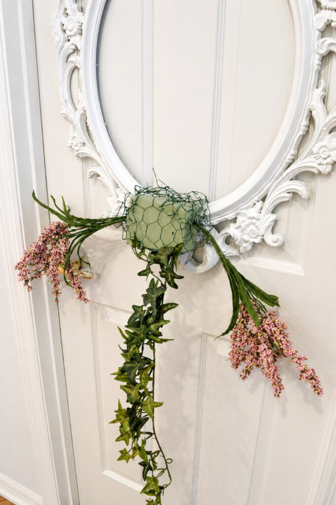 DIY picture frame wreath tutorial showing floral foam attached to an ornate white picture frame with chicken wire before adding flowers and greenery.
