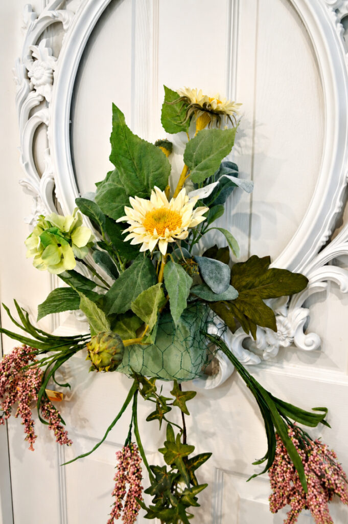 "Adding faux sunflowers, greenery, hydrangea, and artichokes to a DIY picture frame wreath on a white front door for a late summer floral door decoration."