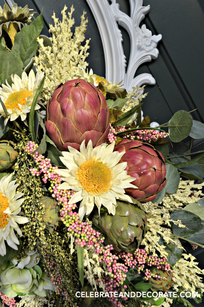 Finished DIY picture frame wreath with faux sunflowers, hydrangea, artichokes, eucalyptus, and cascading greenery arranged inside an ornate white frame on a white front door."