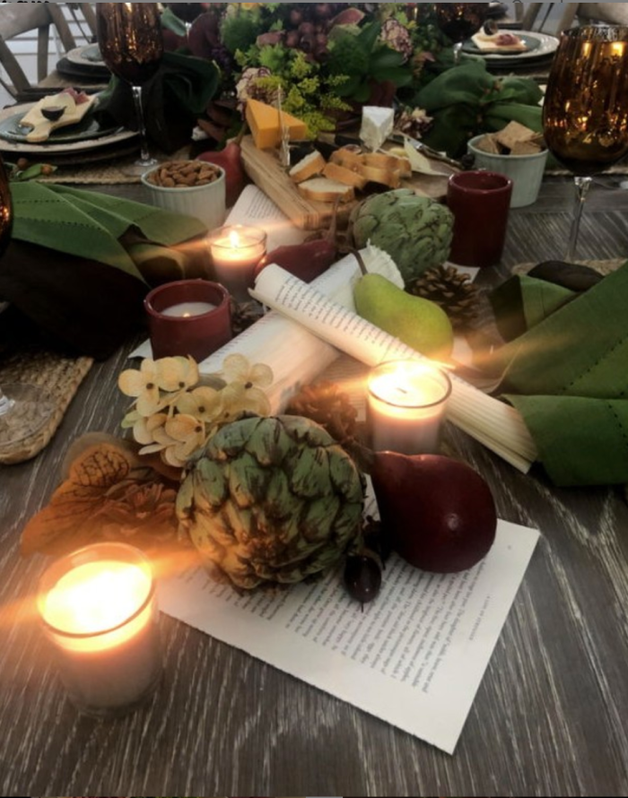 Candlelit late summer tablescape featuring pears, artichokes, greenery, vintage book pages, and a rustic charcuterie board for cozy seasonal entertaining.