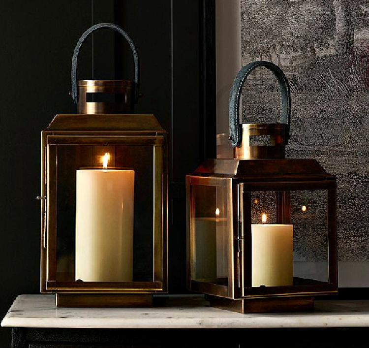 Pair of brass lanterns with glowing pillar candles styled on a marble console table, creating a warm and inviting display for late summer decorating.
