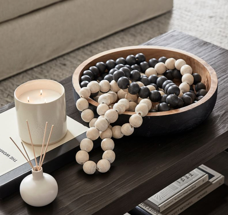 Wood bead garland displayed in a wooden bowl with a candle and reed diffuser on a coffee table for cozy late summer decorating.
