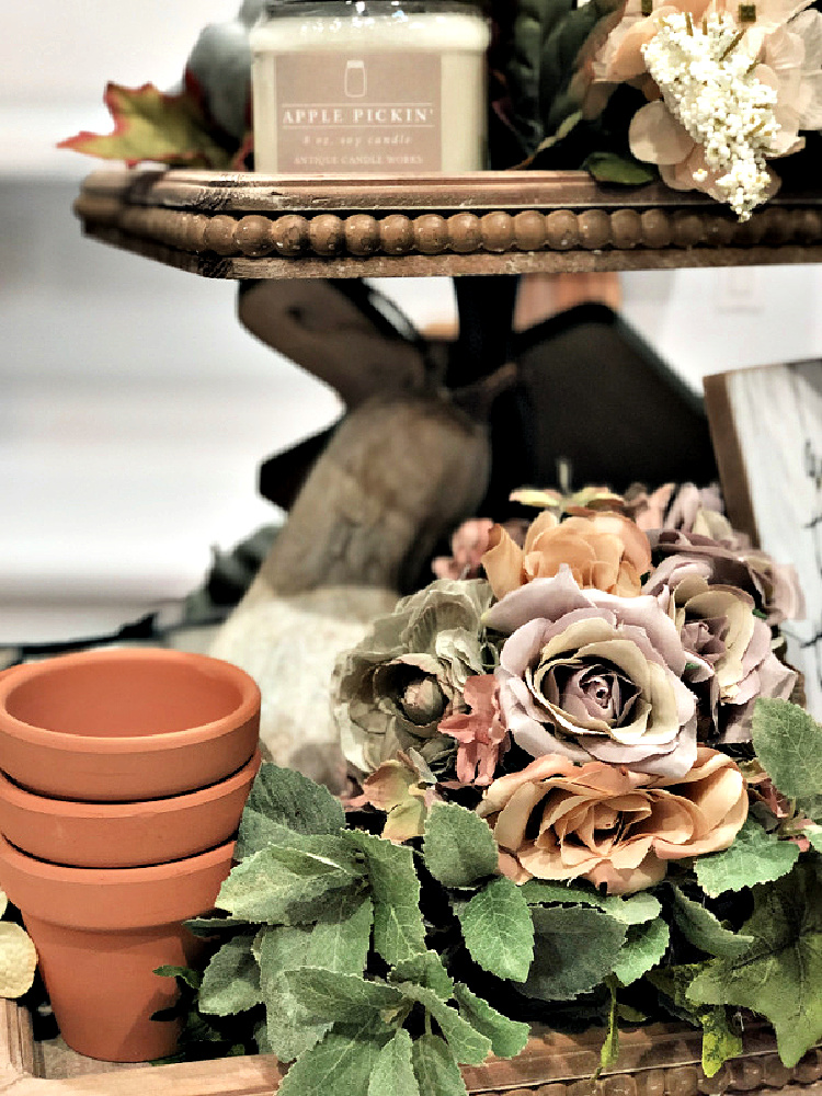 Rustic tiered tray styled with terracotta pots, faux flowers, greenery, and a scented candle for cozy late summer decorating.