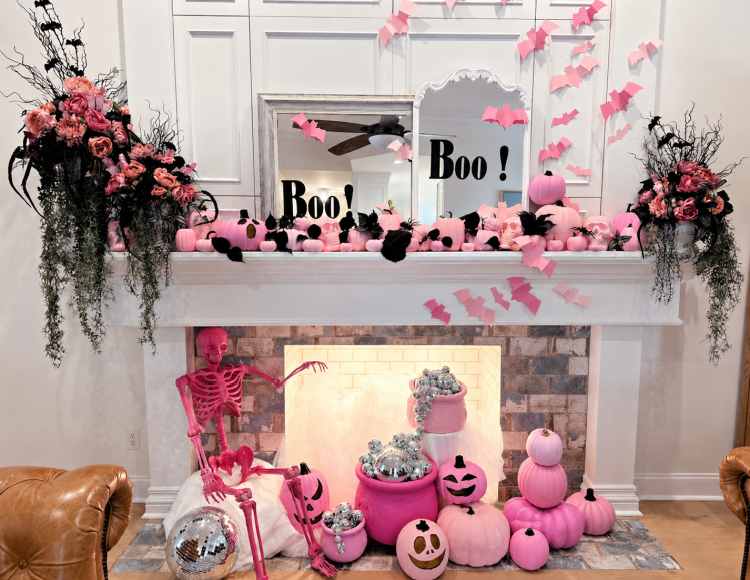 Pink Halloween fireplace mantel decorated with pink pumpkins, paper bats, dark floral arrangements, “Boo!” mirrors, a hot-pink skeleton, and silver disco balls.
