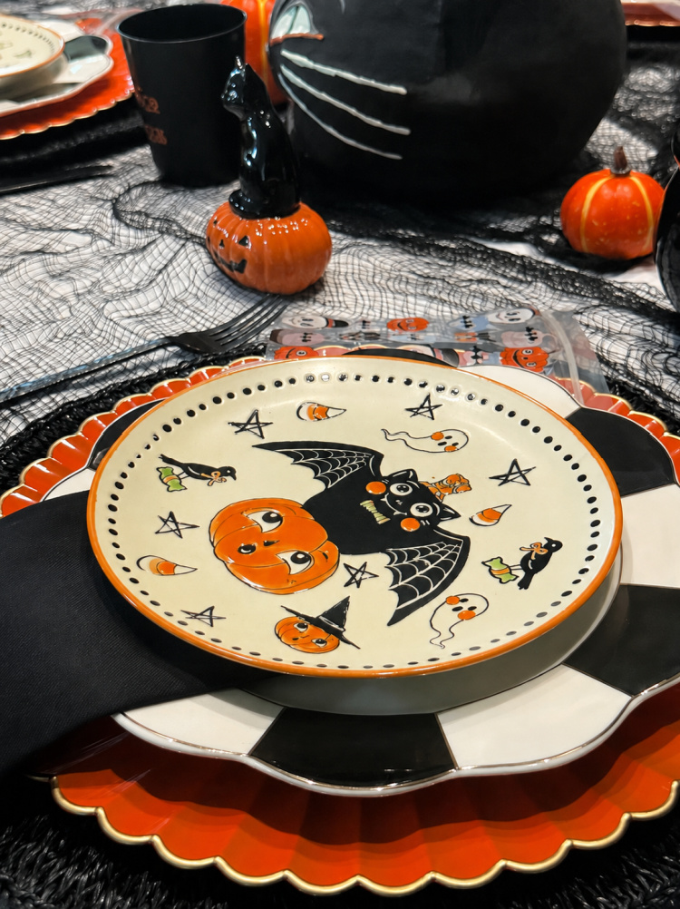 Vintage Halloween place setting with an orange charger, black-and-white checkered dinner plate, and whimsical plate decorated with pumpkins, cats, ghosts, and candy corn.