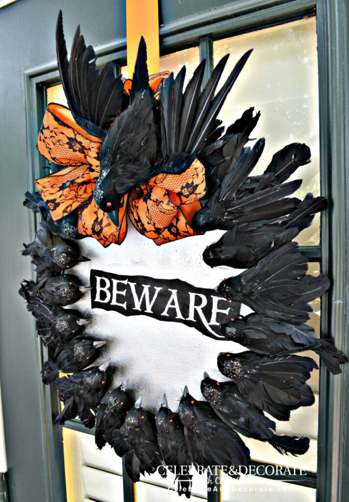Creepy Halloween wreath covered with black crows, an orange-and-black lace bow, and a “Beware” sign displayed on a dark door.