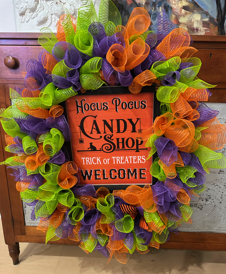 Colorful Halloween deco mesh wreath in orange, purple, and lime green surrounding a “Hocus Pocus Candy Shop—Trick or Treaters Welcome” sign.