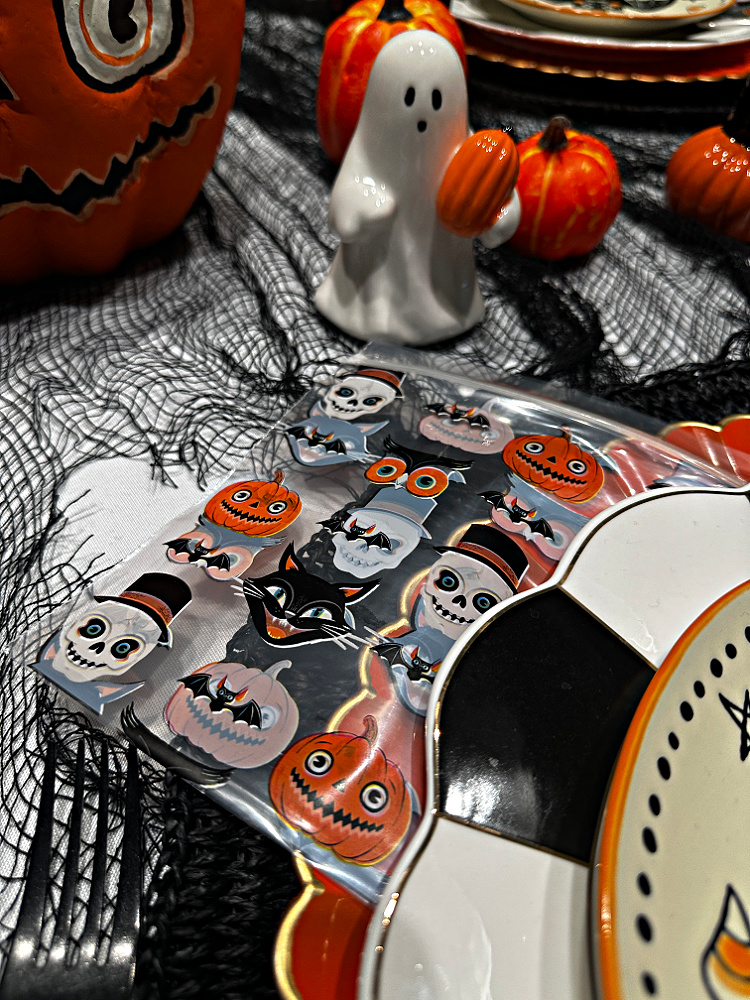 Vintage-style Halloween picture treat bag featuring pumpkins, black cats, bats, and skeletons beside a ceramic ghost and miniature pumpkins.