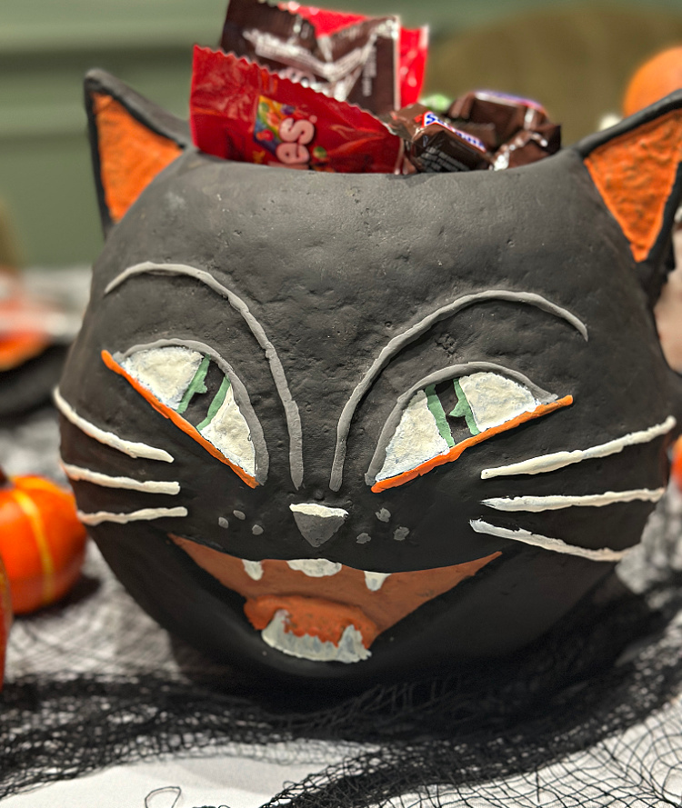 Vintage-style black cat candy bowl filled with assorted wrapped Halloween treats on a decorated table.