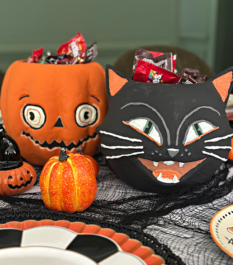 Vintage-style jack-o’-lantern and black cat containers filled with Halloween candy on a festive black-and-orange tablescape.