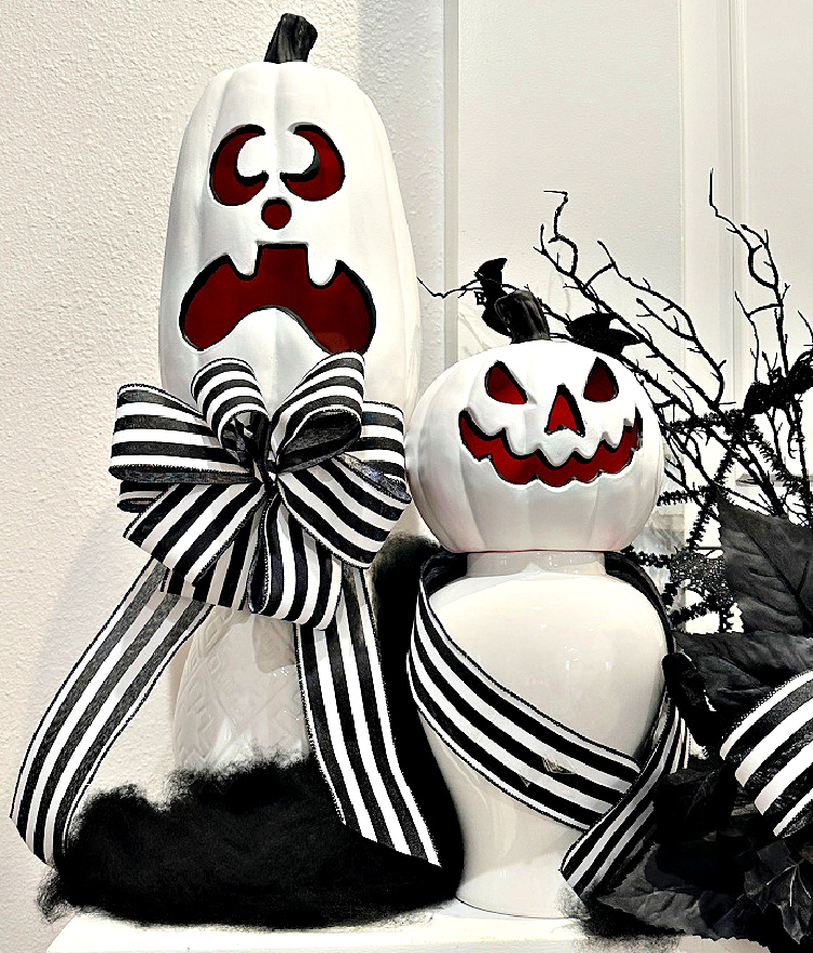 Black-and-white Halloween mantel display with whimsical painted jack-o’-lanterns, striped ribbon, wispy cobwebs, bare branches, and black foliage.