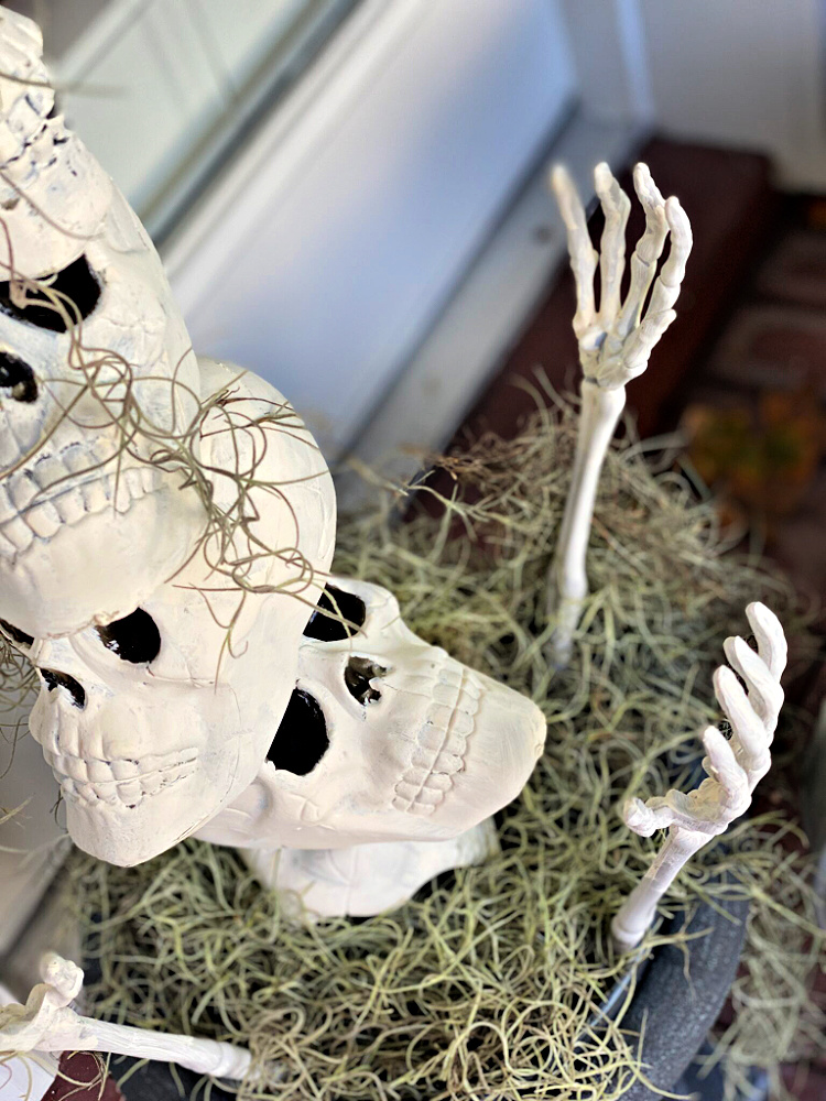Halloween topiary made with stacked white skulls, skeletal hands, and wispy Spanish moss arranged in an outdoor planter.