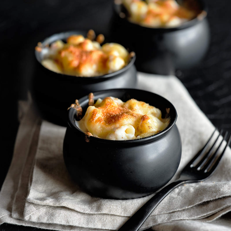 Individual servings of baked macaroni and cheese in small black cauldron bowls on a folded linen napkin.