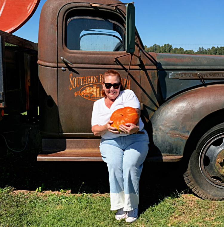 Chloe holding an orange pumpkin in front of a vintage farm truck