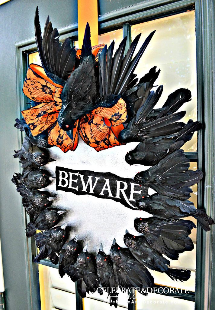 Creepy Halloween wreath covered with black feathered crows, glowing red eyes, an orange-and-black lace bow, and a weathered “Beware” sign.