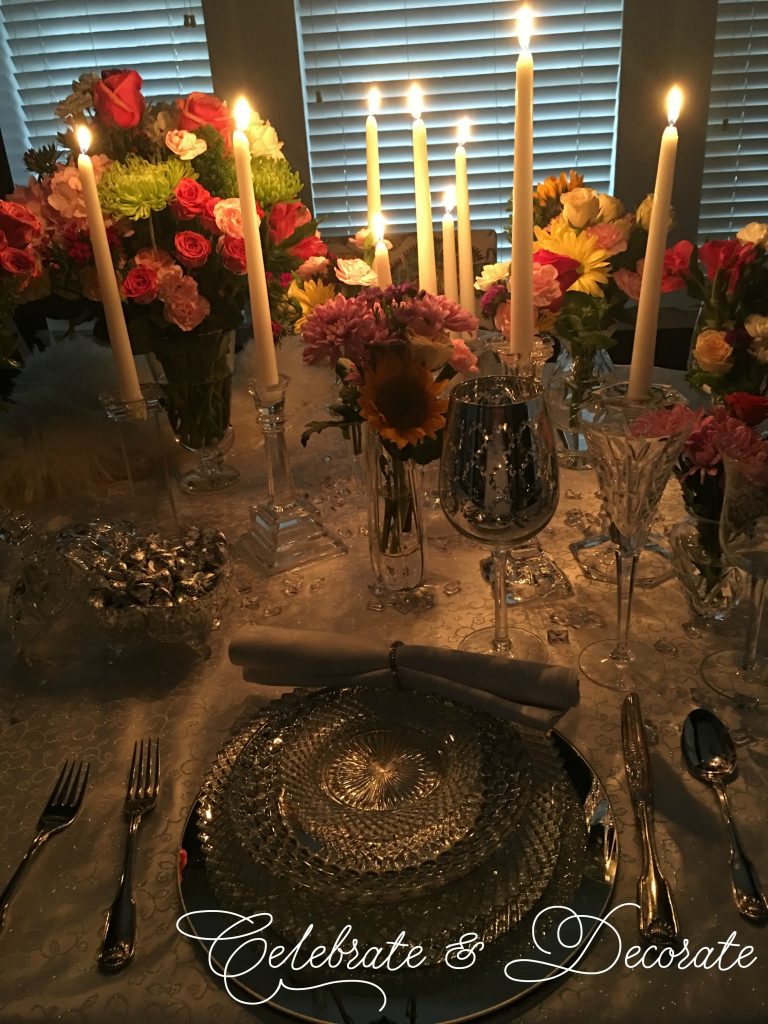 Colorful roses, carnations, and chrysanthemums arranged among glowing white taper candles in clear glass holders.