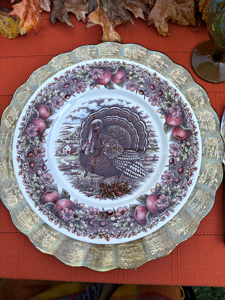 Royal Stafford turkey dinner plate with a fruit, flower, and acorn border, layered over a scalloped gold-toned charger on a rust tablecloth.