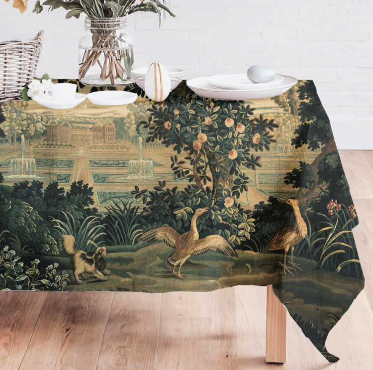 Green and gold tablecloth featuring an ornate garden scene with birds, flowers, and trees, styled with white dishes and a vase of flowers.
