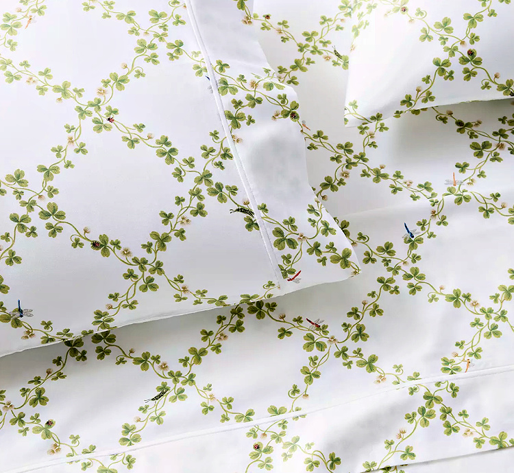 White sheets and pillowcases patterned with winding green clover vines, tiny flowers, and colorful insects.